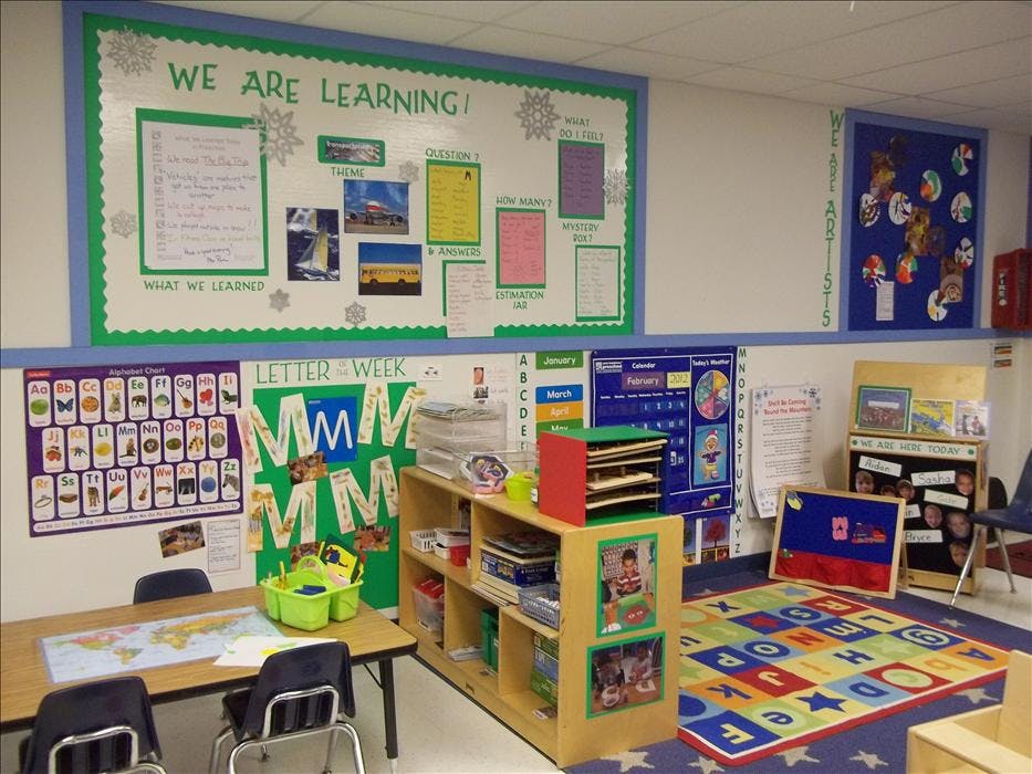 Classroom with learning charts, alphabet poster, bookshelf, small tables, and alphabet rug