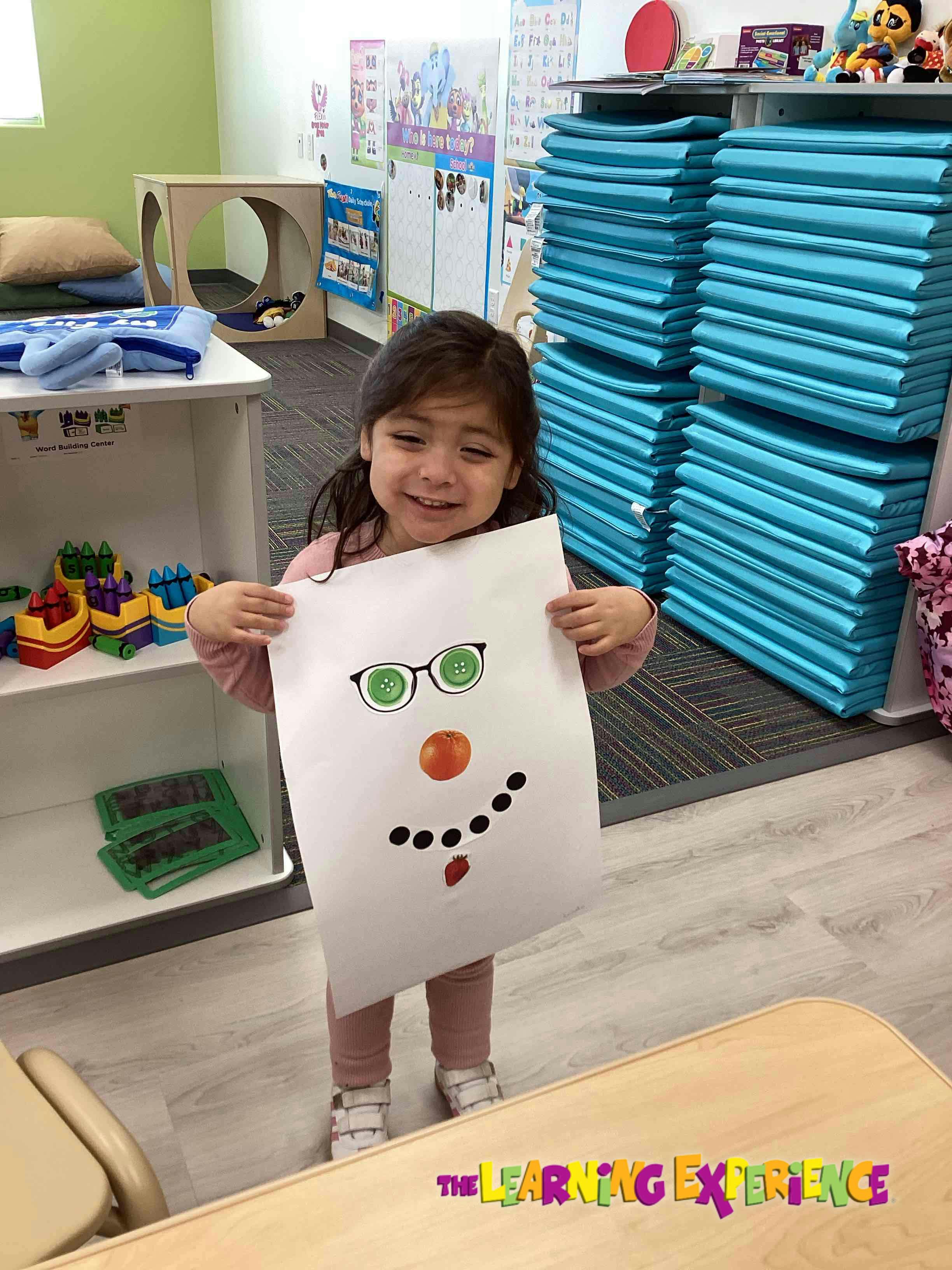 Child holding up a drawing of a face with green glasses