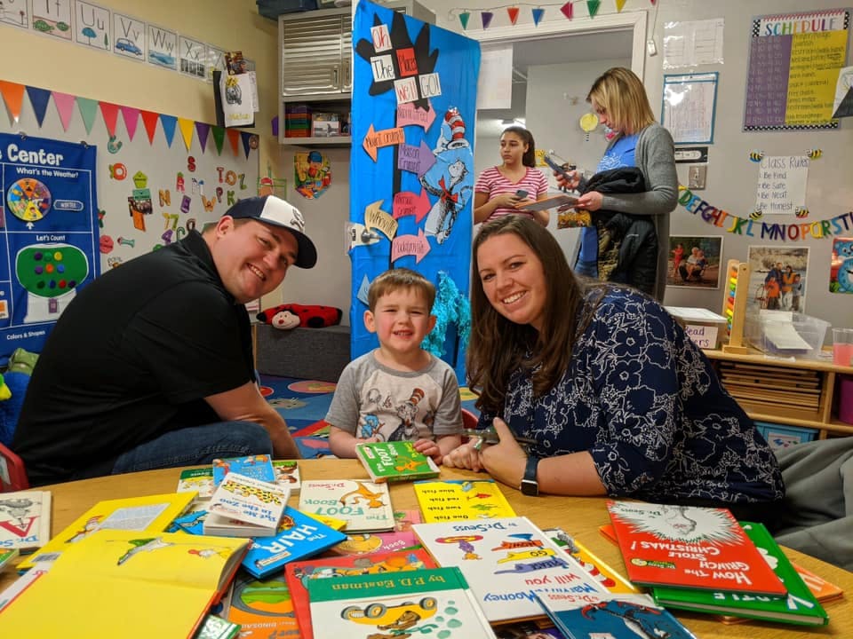 Adults and a child sitting at a table with books in a classroom