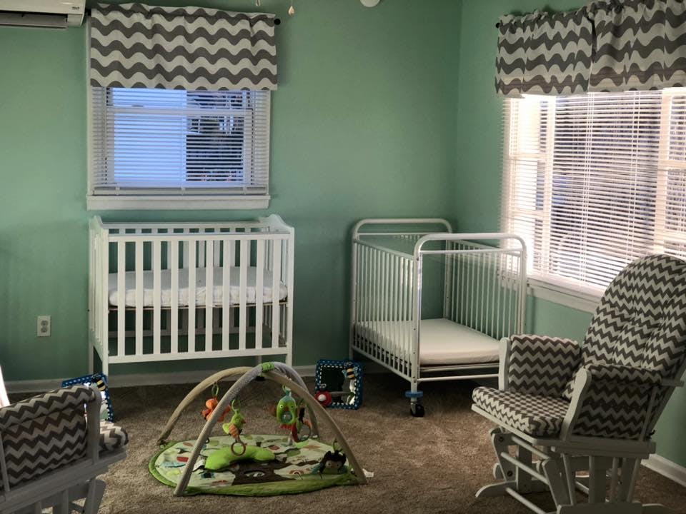 Two cribs, a play mat, and a rocking chair in a room