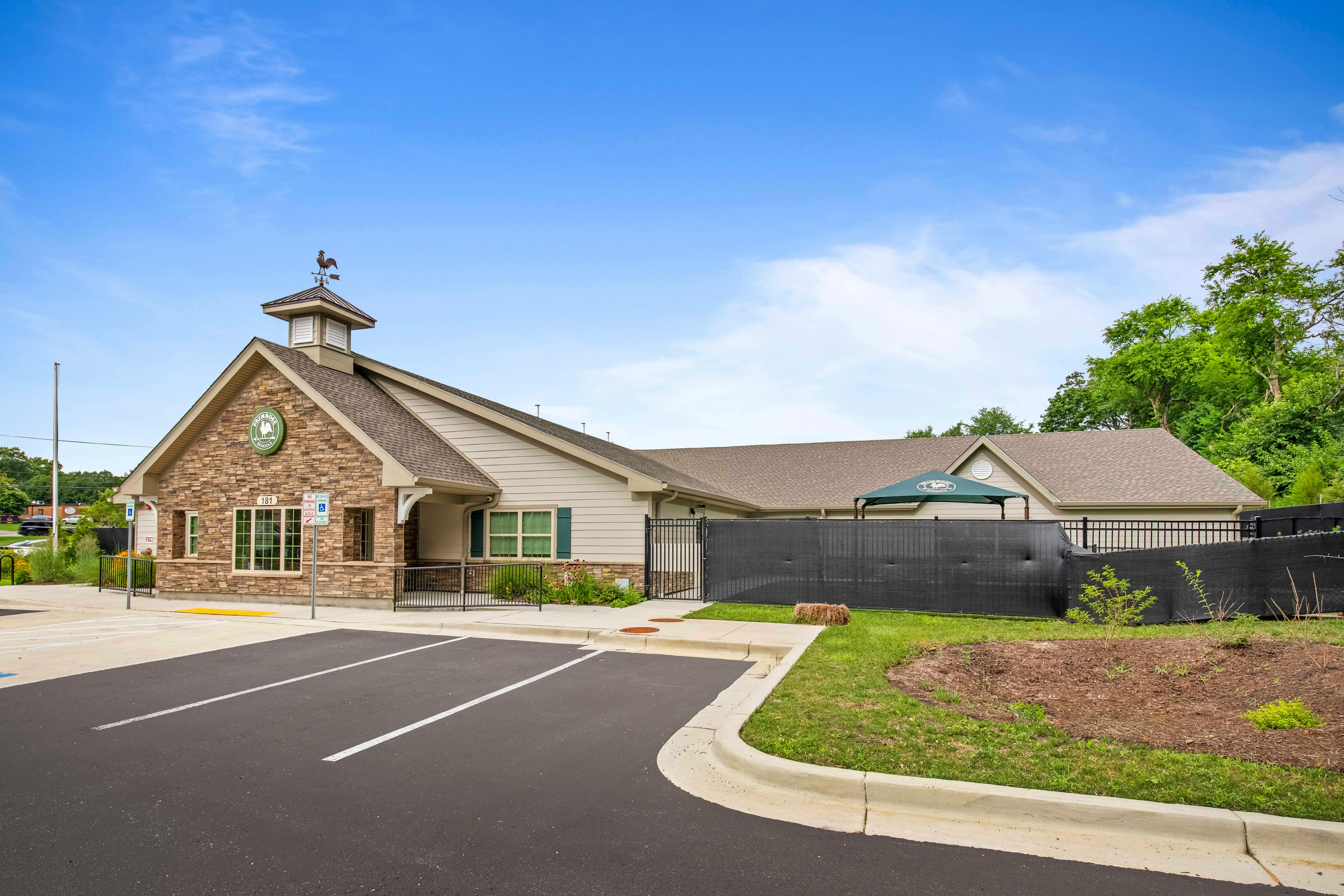 A beige building with stone facade, cupola and rooster weather vane, and a paved parking lot