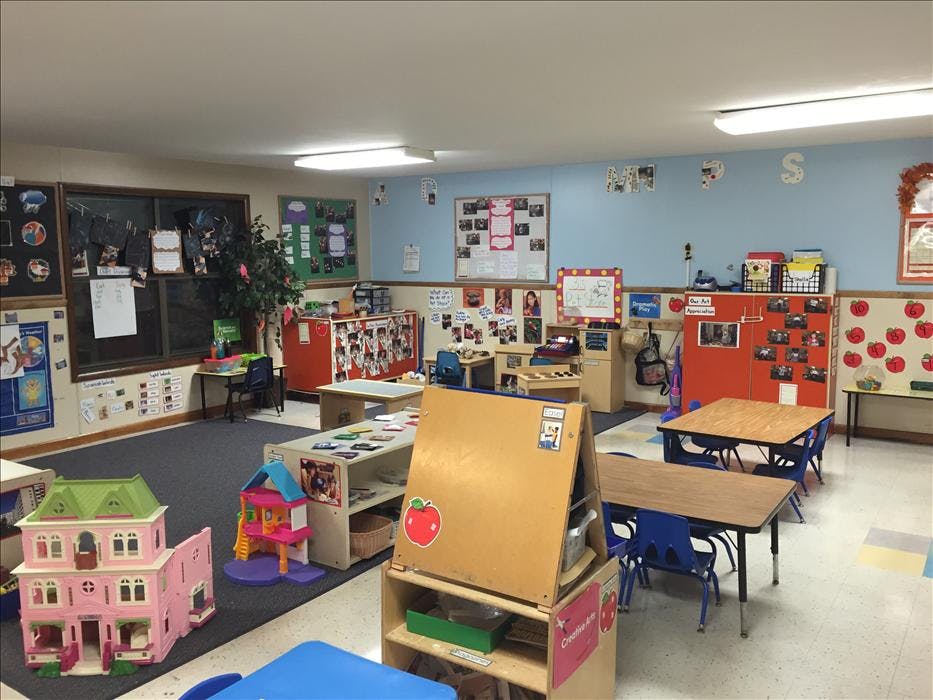 An empty early childhood classroom with toys, tables, and art on the walls