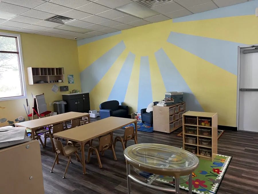 Classroom with tables and chairs, sun mural on wall