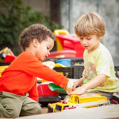 Two children playing with toy trucks in sand