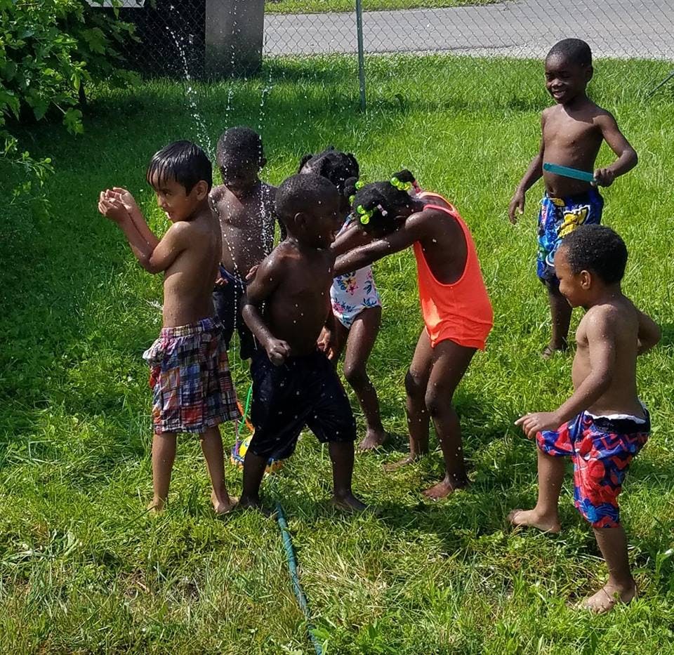 Children playing in water from a sprinkler on a grassy lawn
