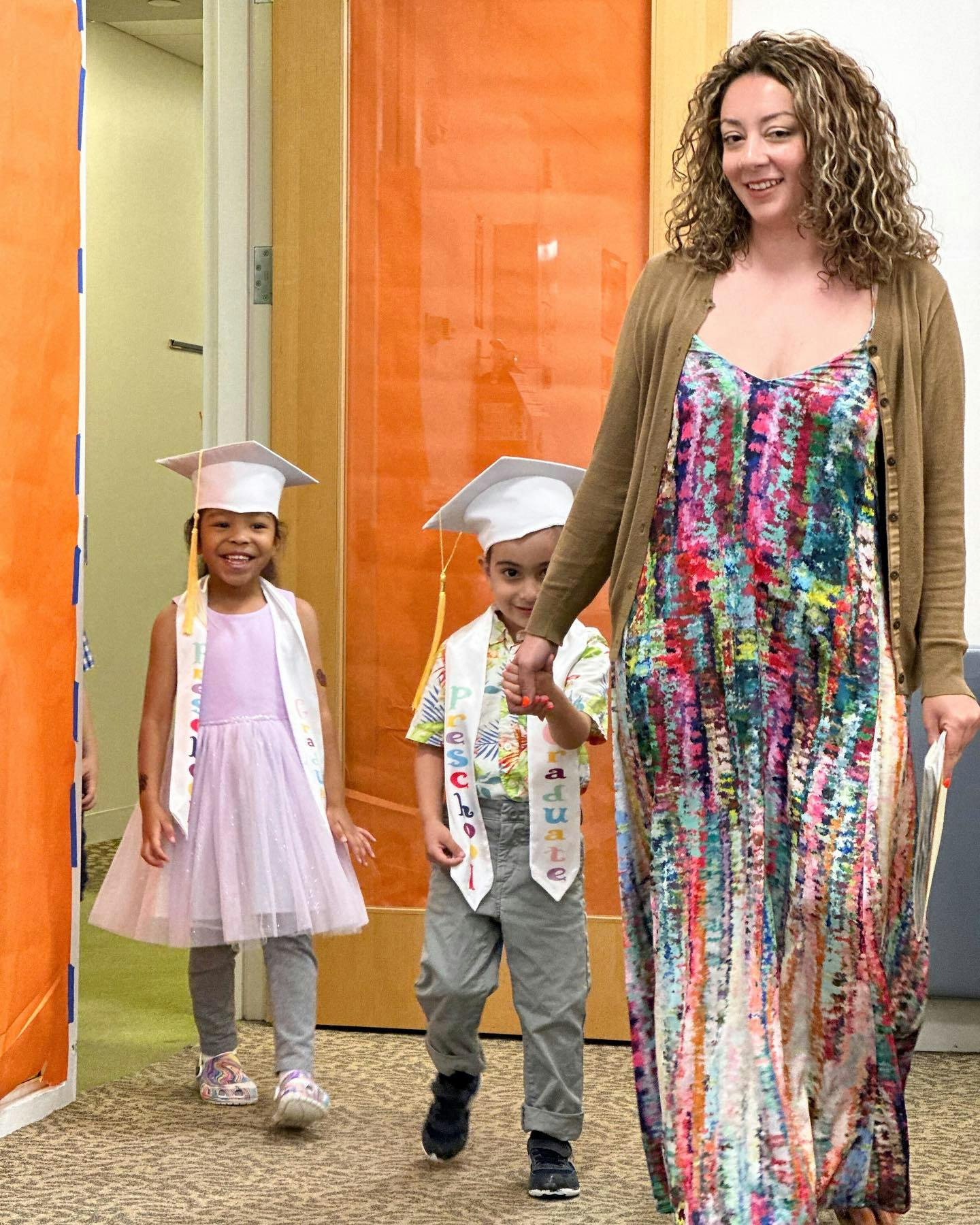 Adult and two children in graduation caps and sashes walking