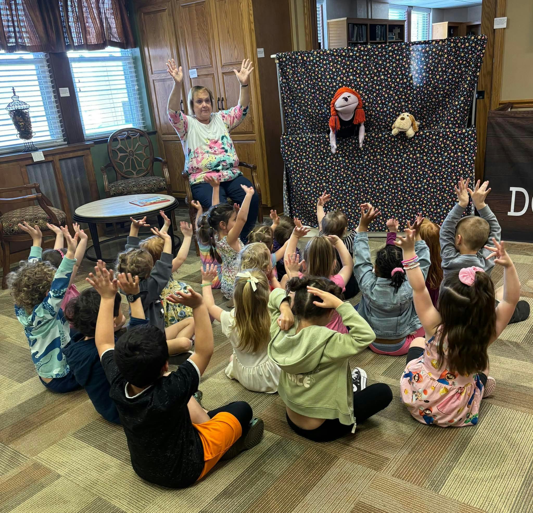 Adult leading children in a circle raising their hands during a puppet show