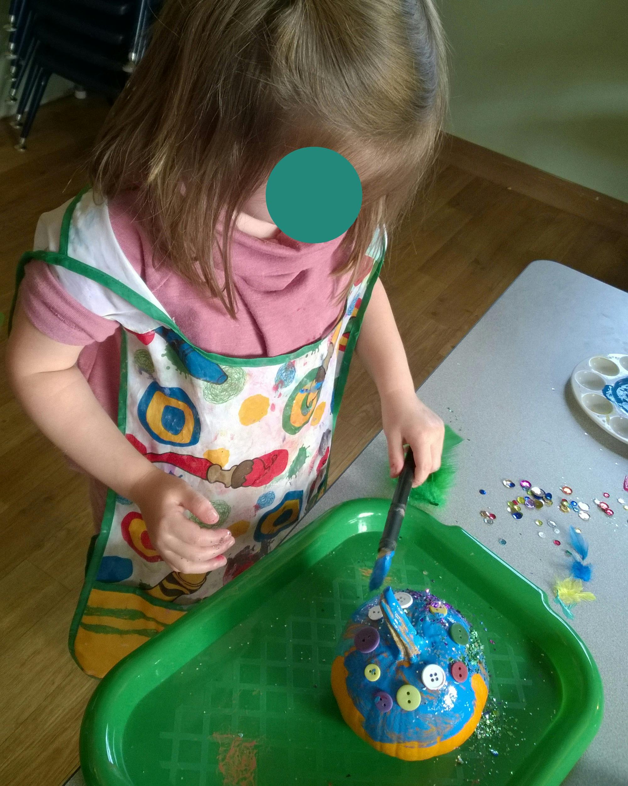 Child wearing an apron painting and decorating a craft project