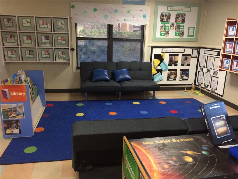 Classroom reading corner with a black sofa, blue rug, and book displays