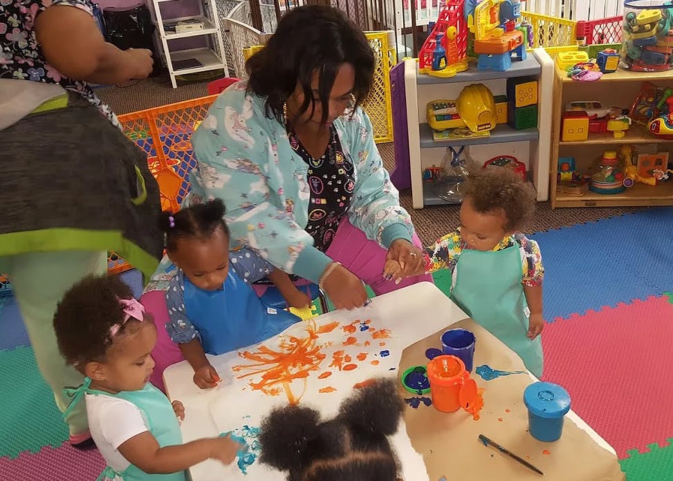Adult and children painting at a table in a classroom