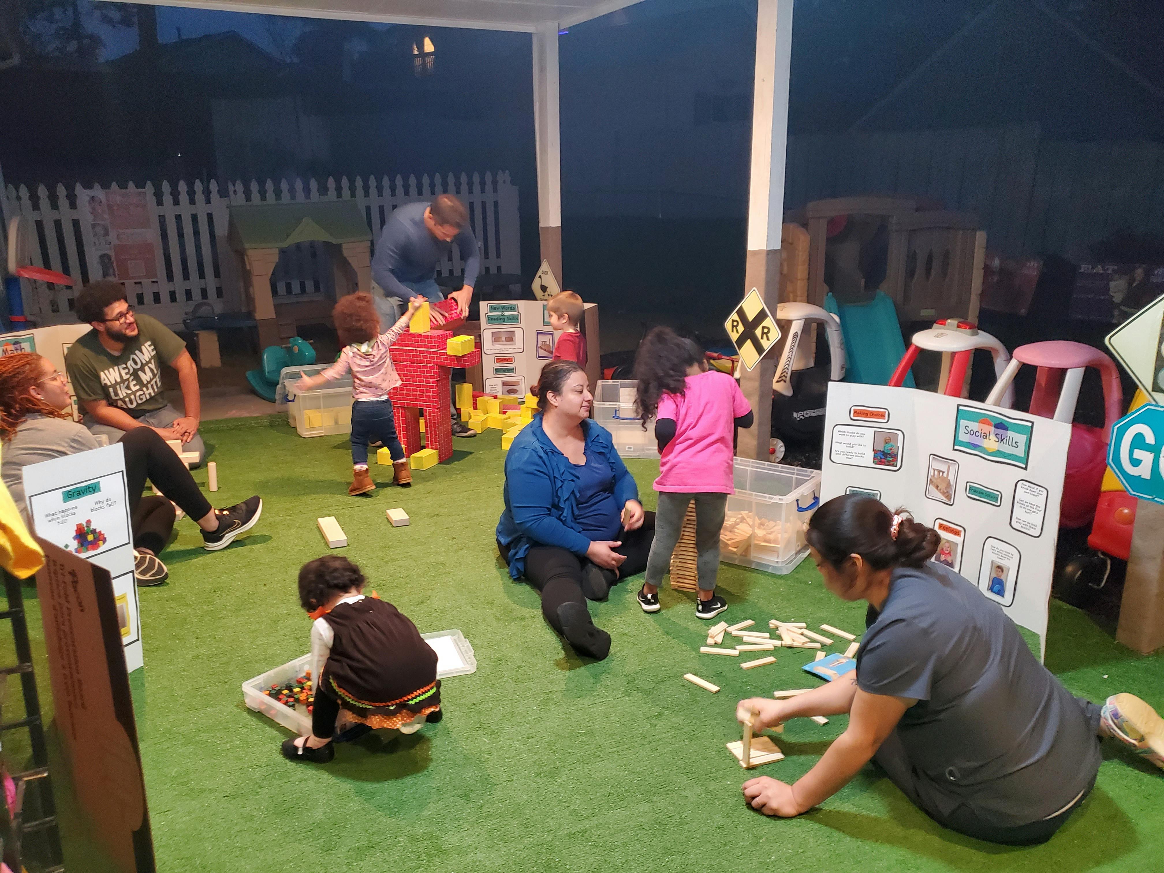 Adults and children playing with toys on a green mat
