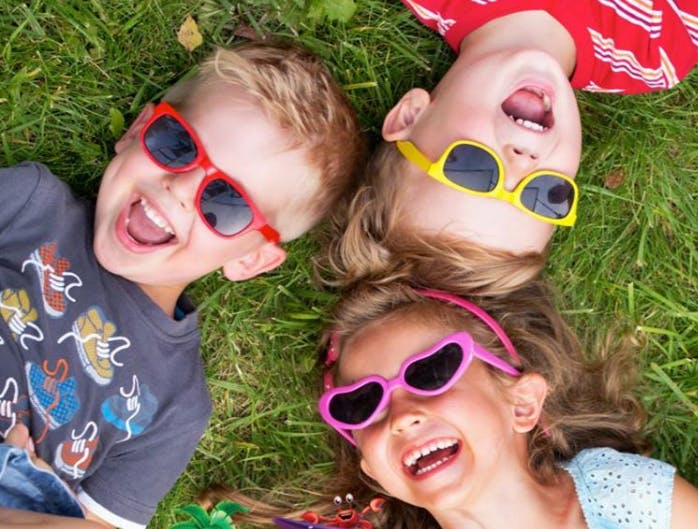 Three children wearing sunglasses lying on grass