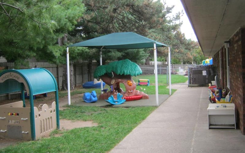 Outdoor play area with a canopy, playhouse, and rocking toys next to a building