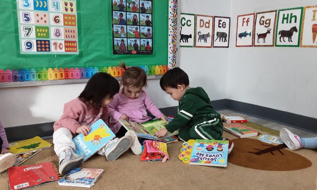 Three children sitting on the floor, reading books in a classroom
