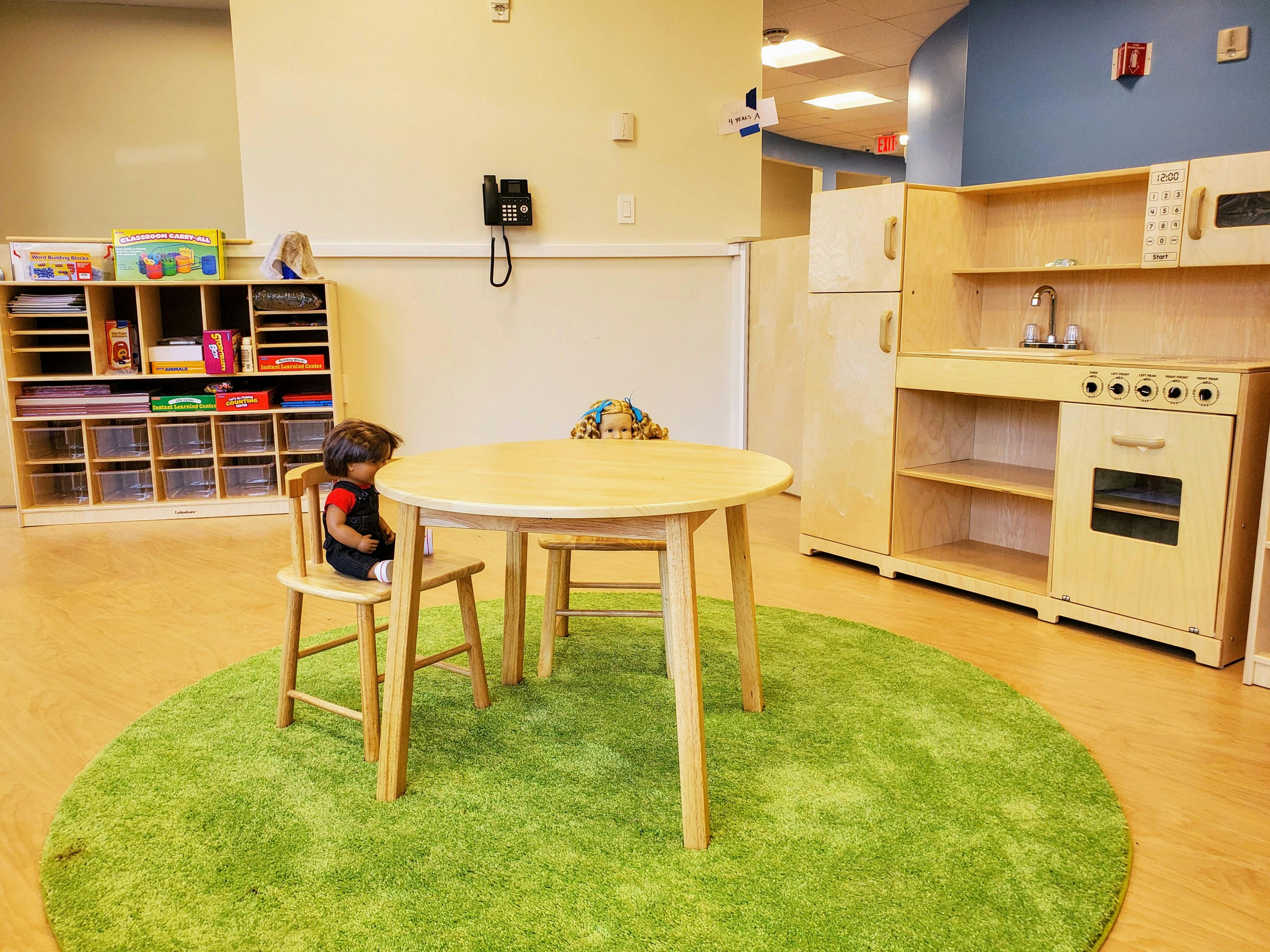 Child sitting at a small wooden table on a green rug in a play area