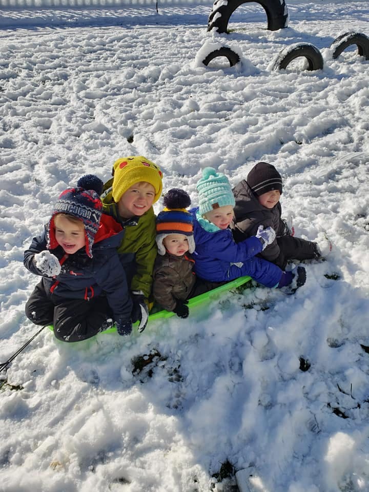Five children sitting on a green sled in the snow