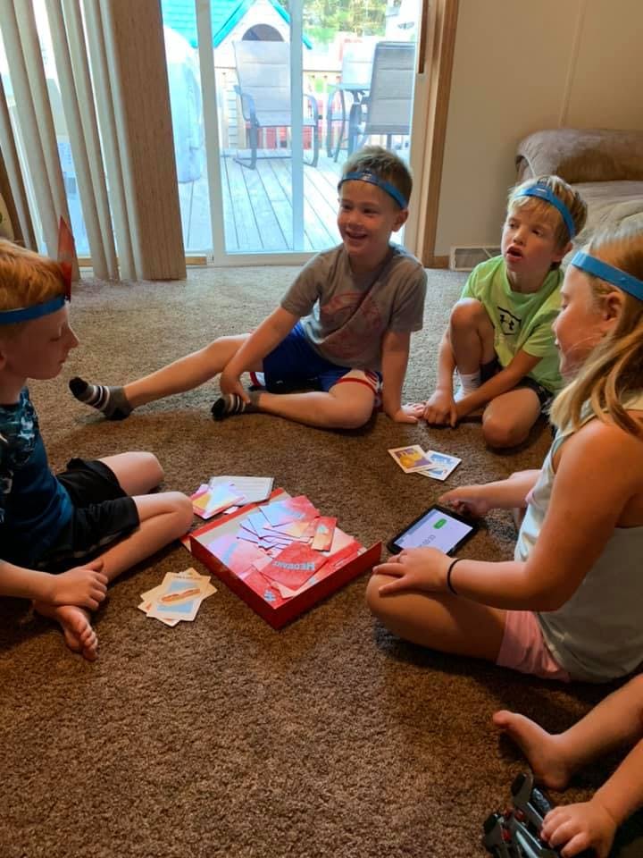 Four children sitting on a carpeted floor playing a game with cards and a tablet