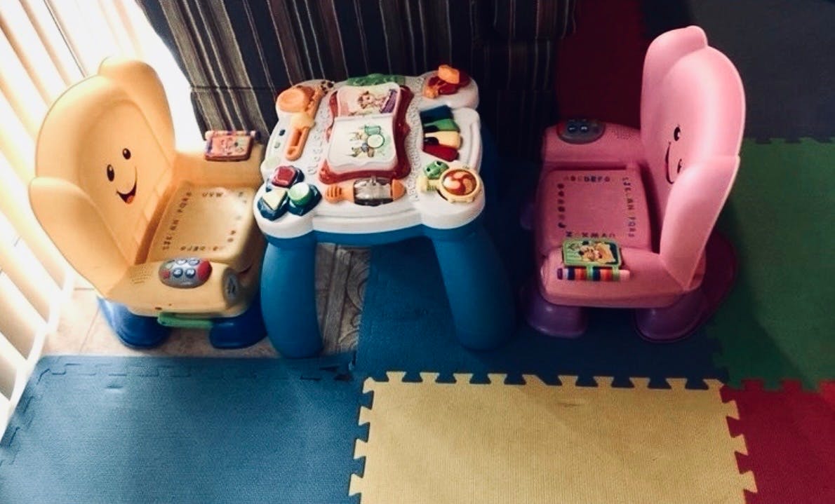 two children's learning chairs with an activity table between them on a foam mat