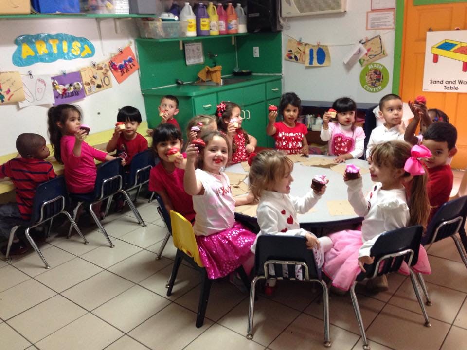 Children sitting at tables holding cupcakes in a classroom