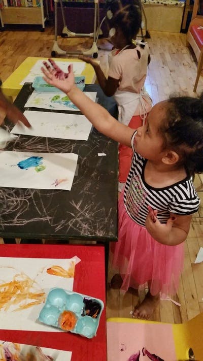 Child with paint on hand reaching out, another child painting in background