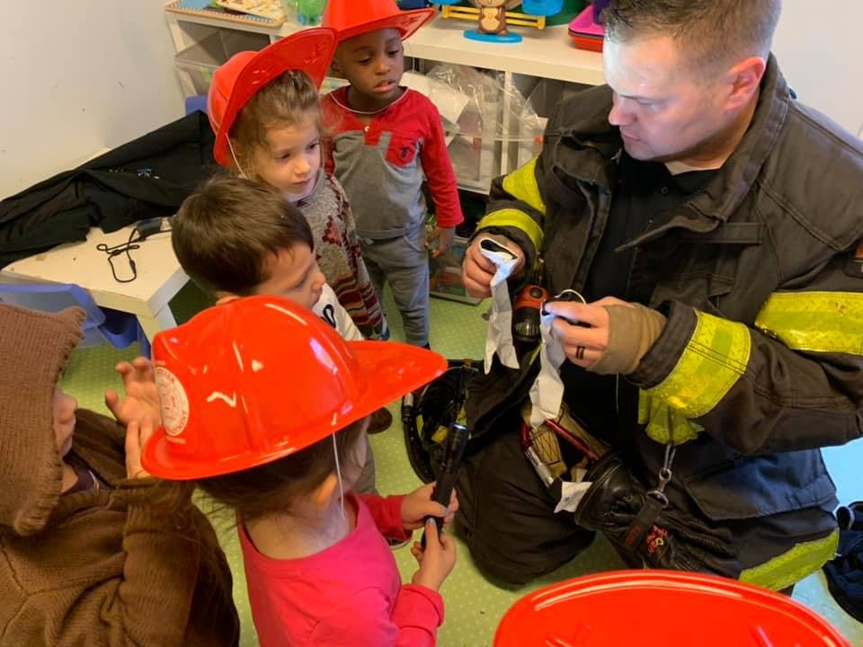 Firefighter showing equipment to children wearing fire hats