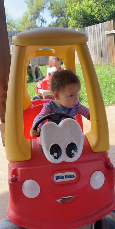 Child in a toy car with another child in a toy car in the background