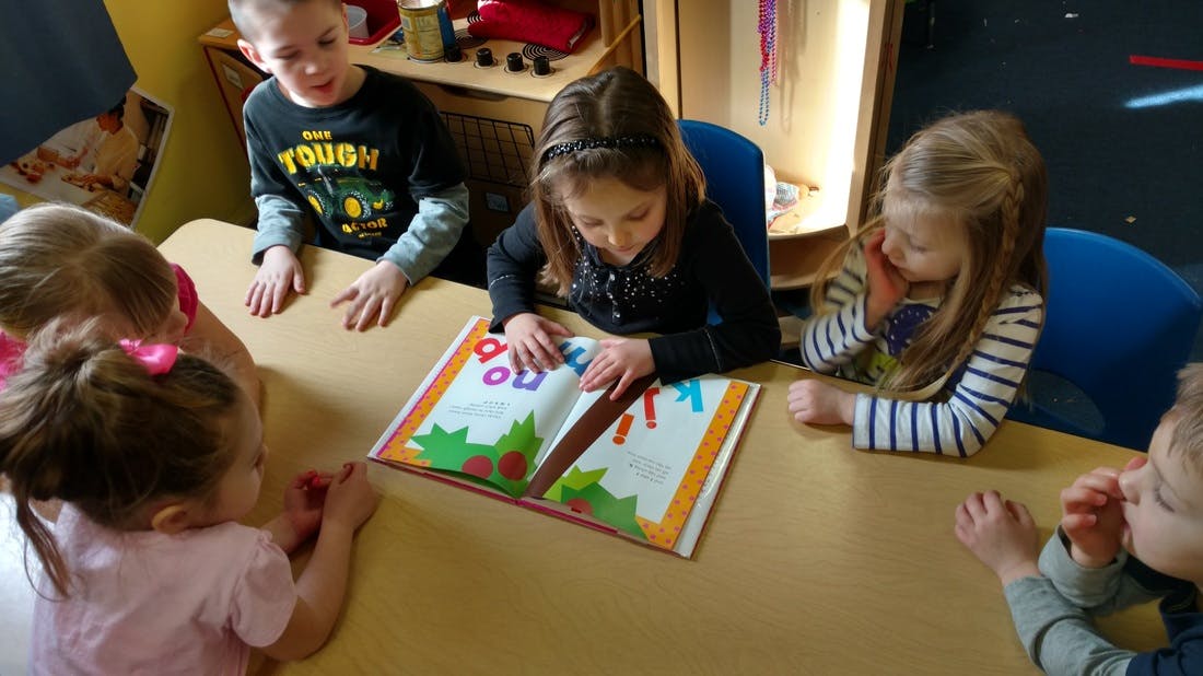Children gathered around a table looking at a book