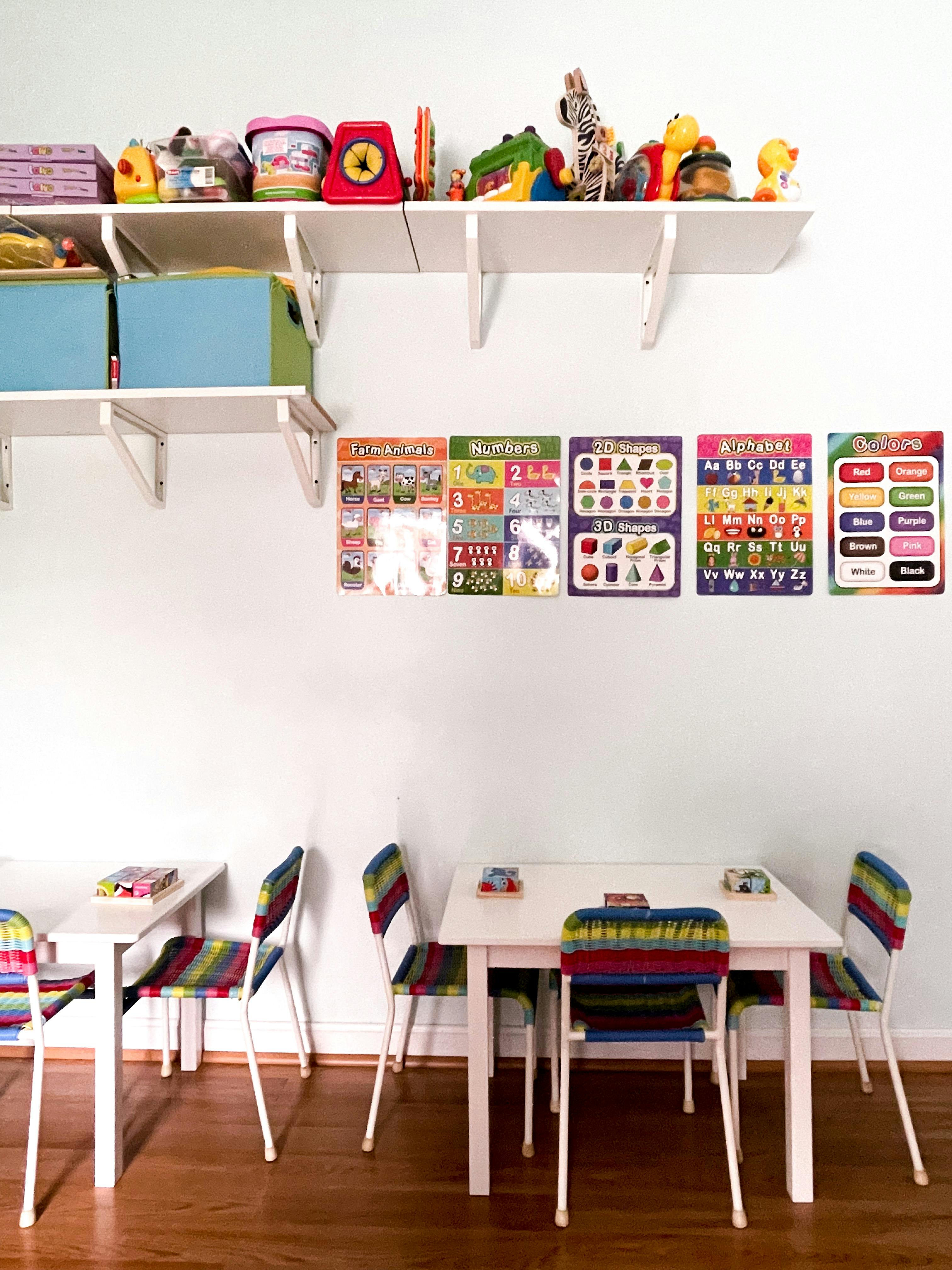 Classroom with small tables and chairs, shelves with toys, and educational posters