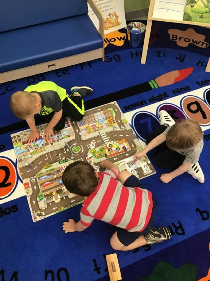 Three children playing with a road map rug on the floor