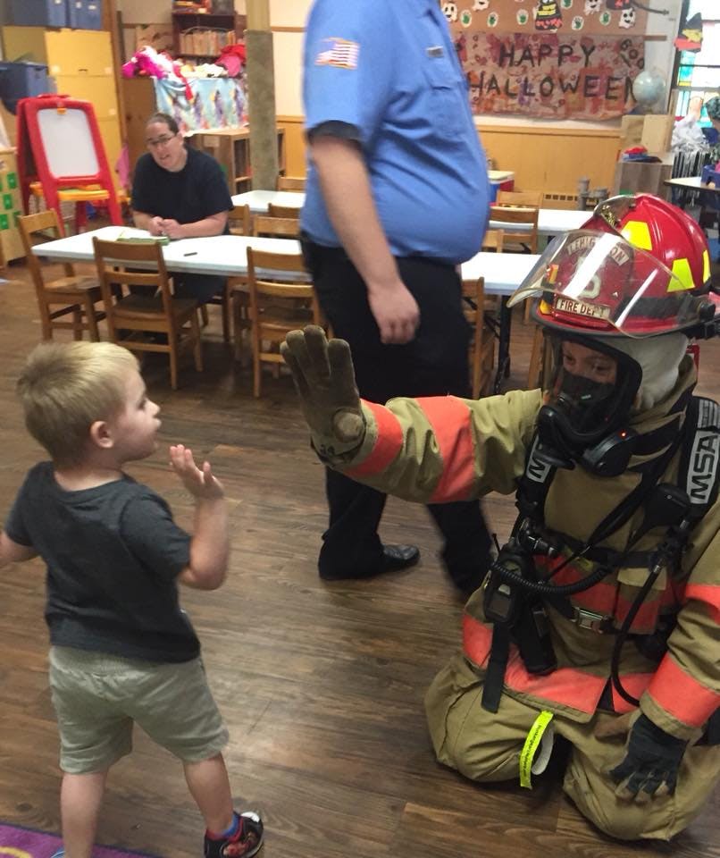 Child looking at person in firefighter gear with helmet and mask