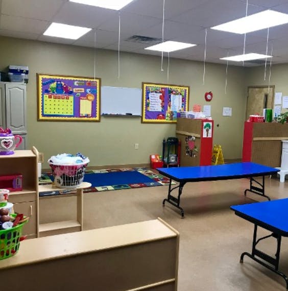 Empty classroom with blue tables, colorful rugs, and bulletin boards