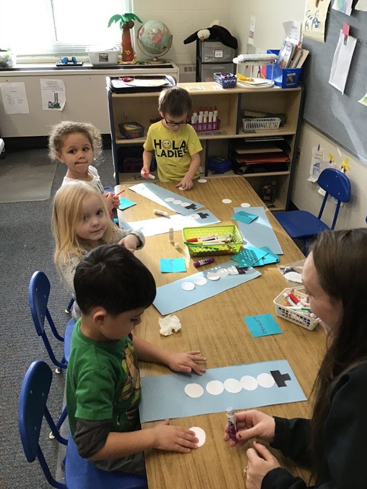 Children and an adult doing crafts at a table in a classroom