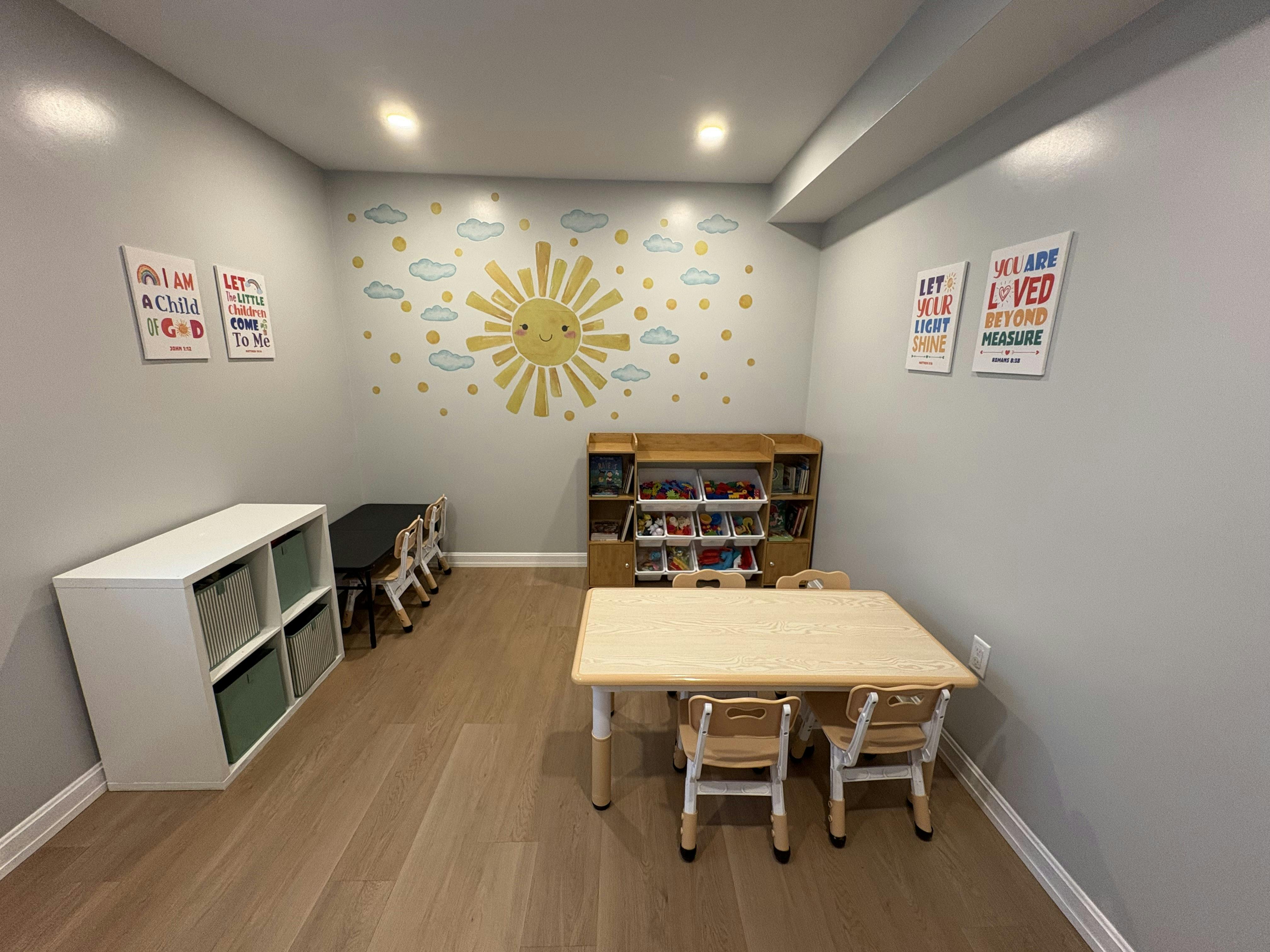 Playroom with tables and chairs for children with sun mural on wall
