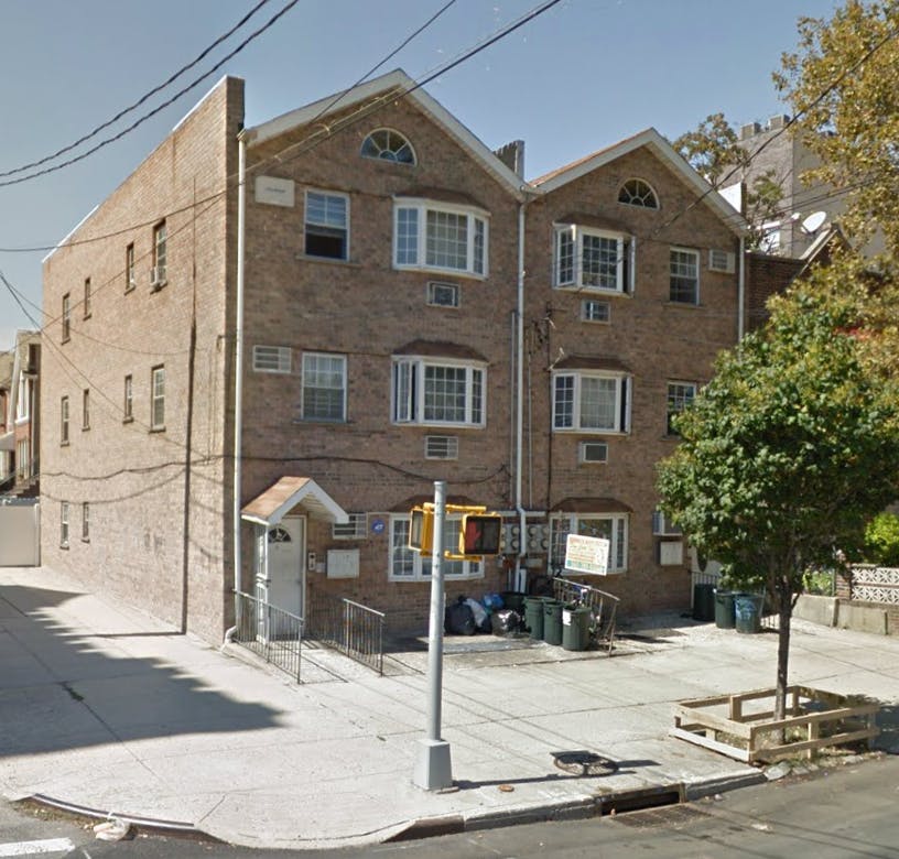 Brick apartment building with bay windows and a small tree on the sidewalk
