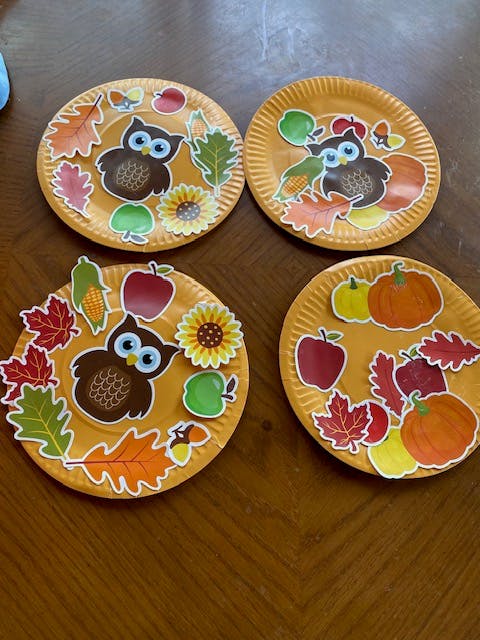 Four paper plates decorated with owl, leaf, and pumpkin stickers