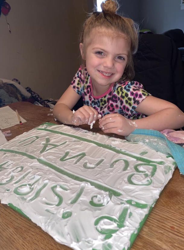 Child with hands covered in white substance, smiling at a craft project