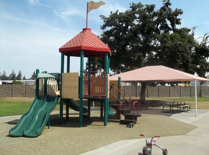 Playground structure with two green slides and a red roof, a shade canopy, and a picnic table