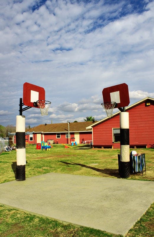 Two basketball hoops on a grassy area with buildings in the background