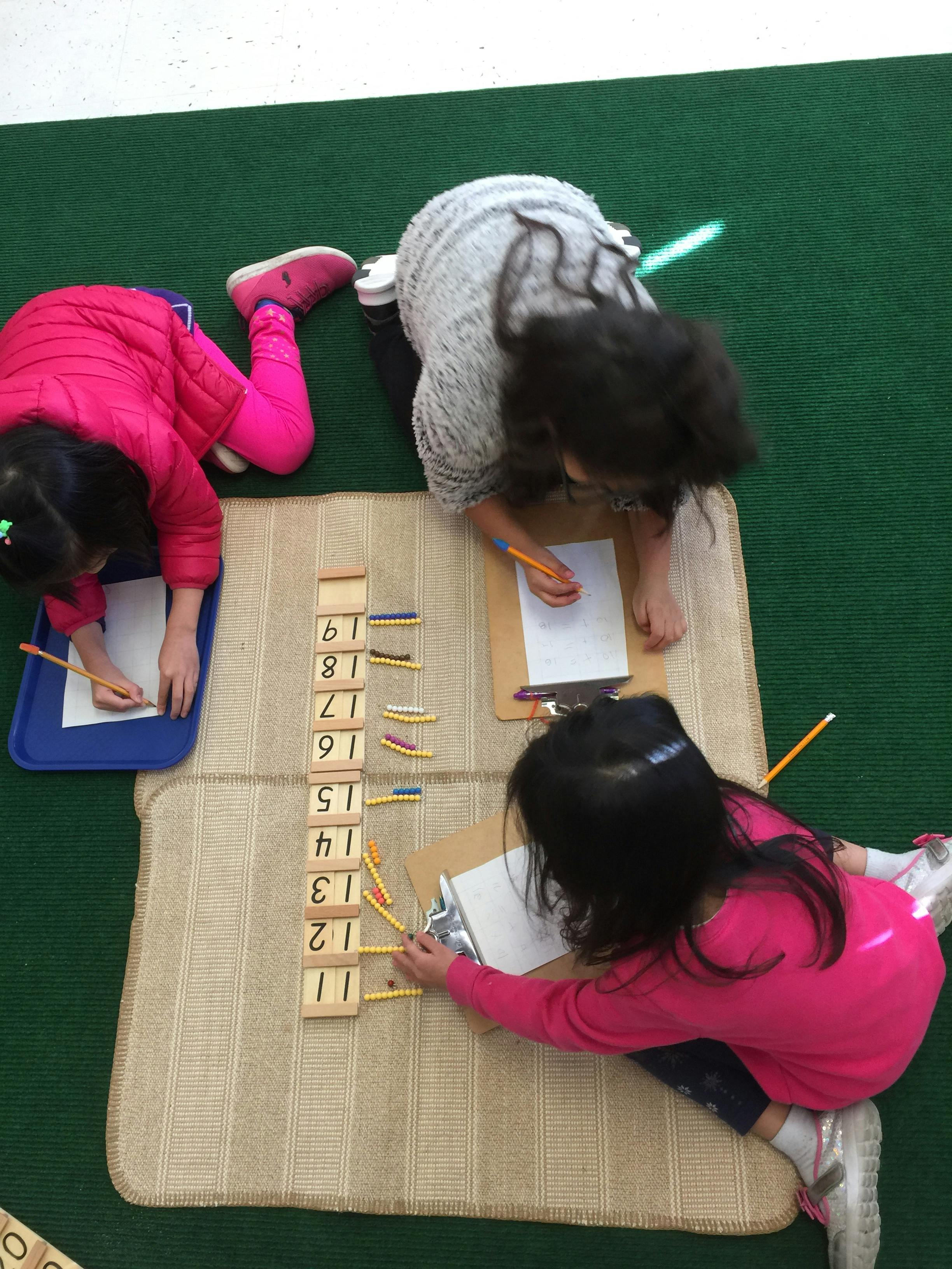 Three children writing and working with number blocks on the floor