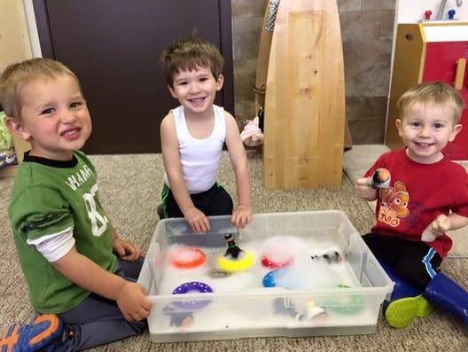 Three children playing with a sensory bin filled with water and toys