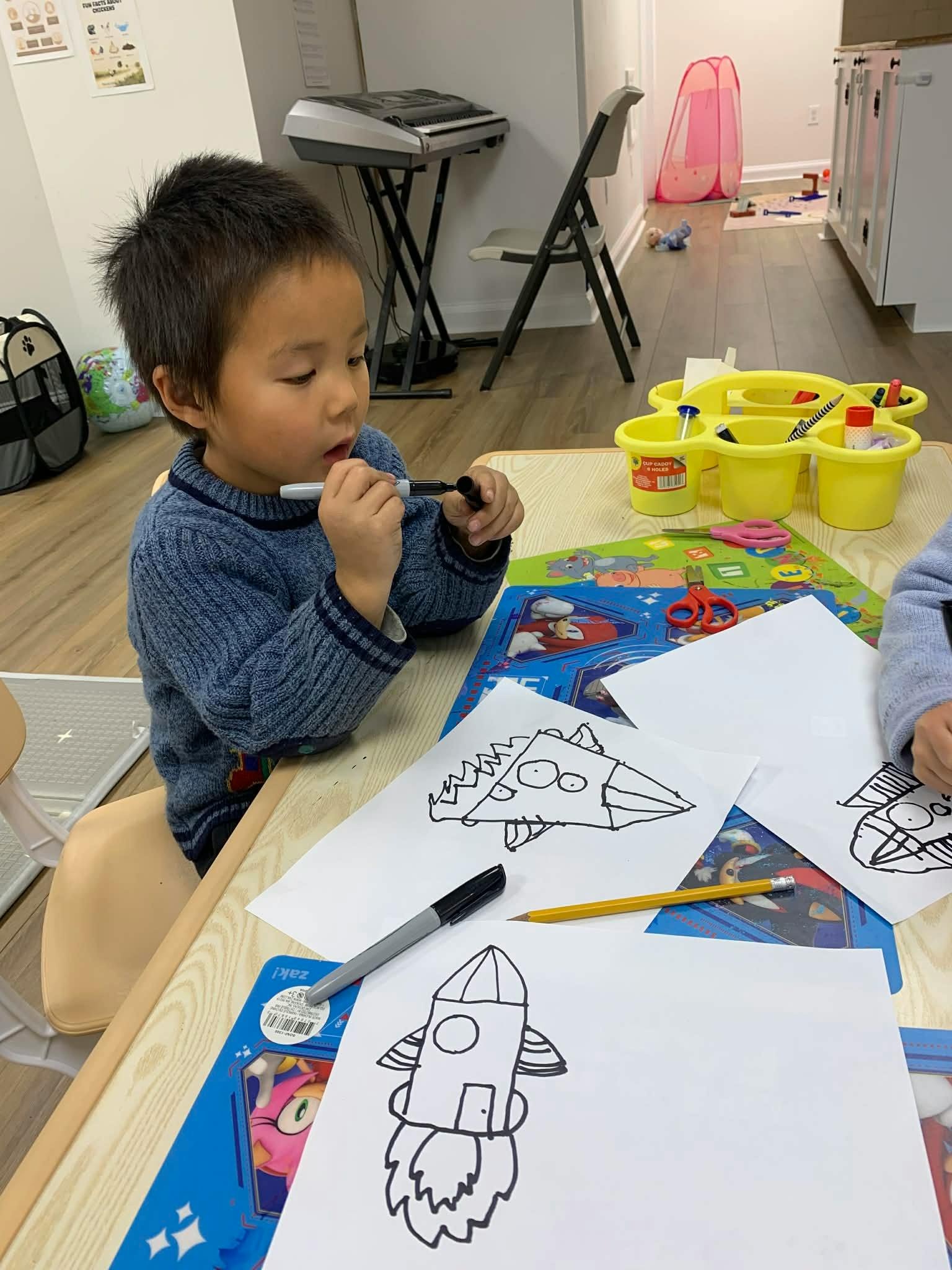 Child drawing with a marker at a table with other drawings