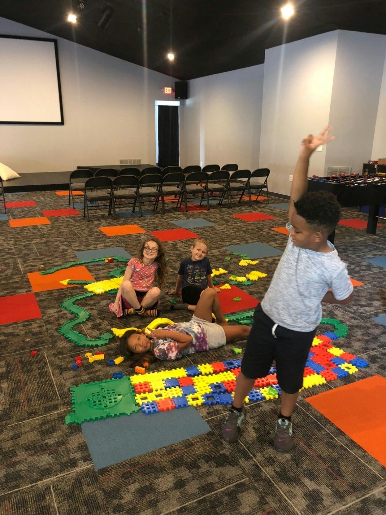 Four children playing on a carpeted floor with colorful interlocking mats