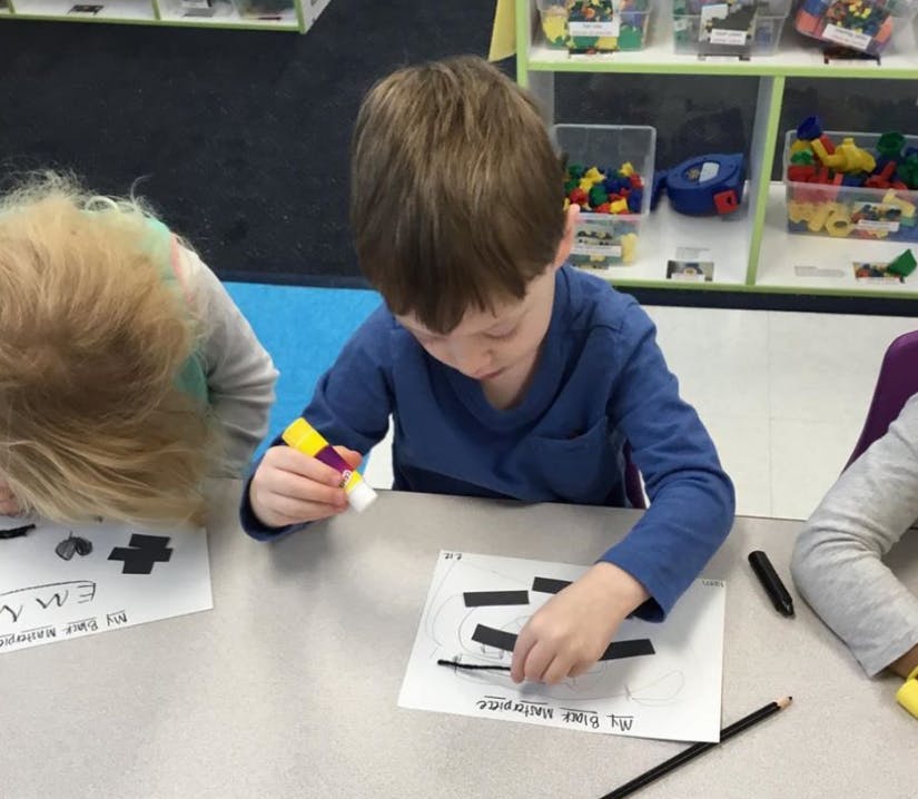 Child gluing paper shapes onto a worksheet at a table