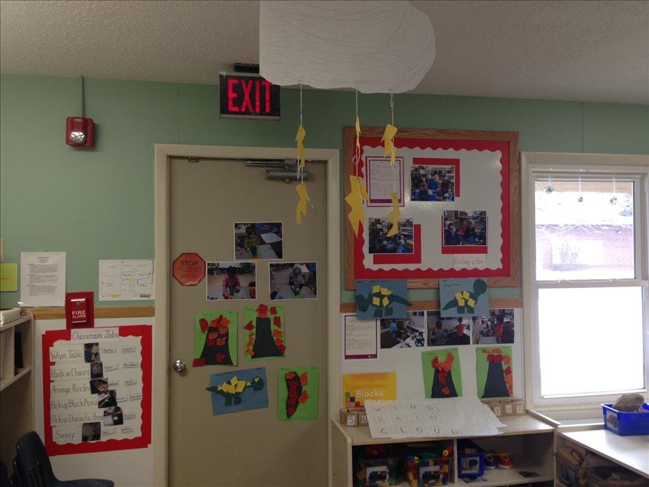 Classroom wall with child artwork, job chart, photos, and exit sign