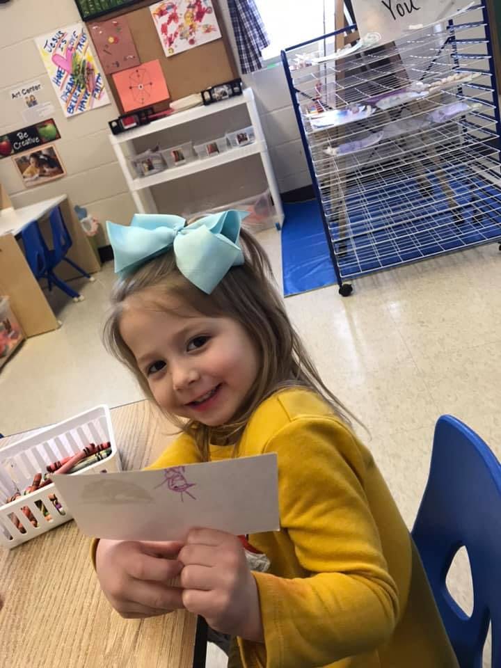 Child in a classroom holding up a piece of paper