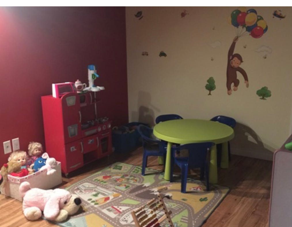 Playroom with a small green table and blue chairs, toys, and wall decals