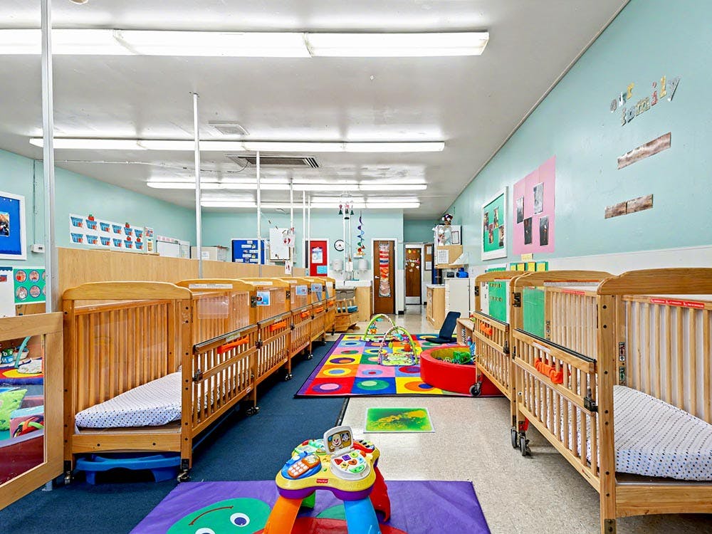 Rows of wooden cribs in a room with a colorful play mat