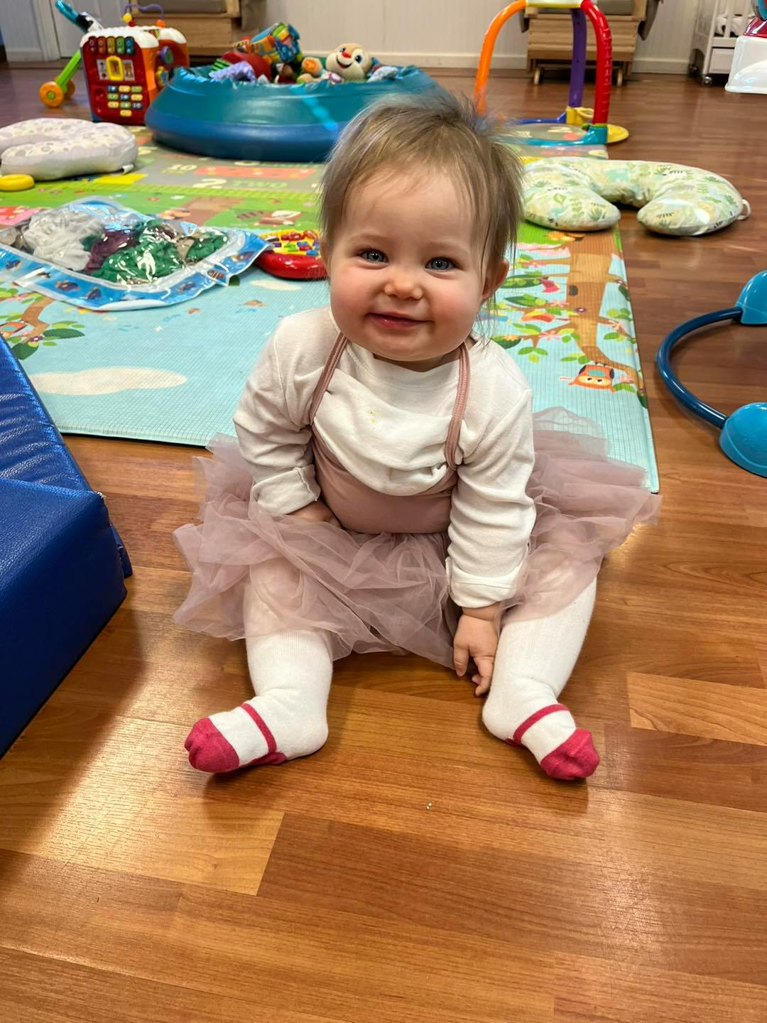 Child sitting on a wooden floor wearing a tutu