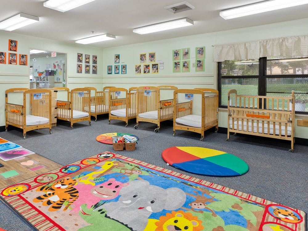 A classroom with several cribs on wheels and colorful animal-themed rugs