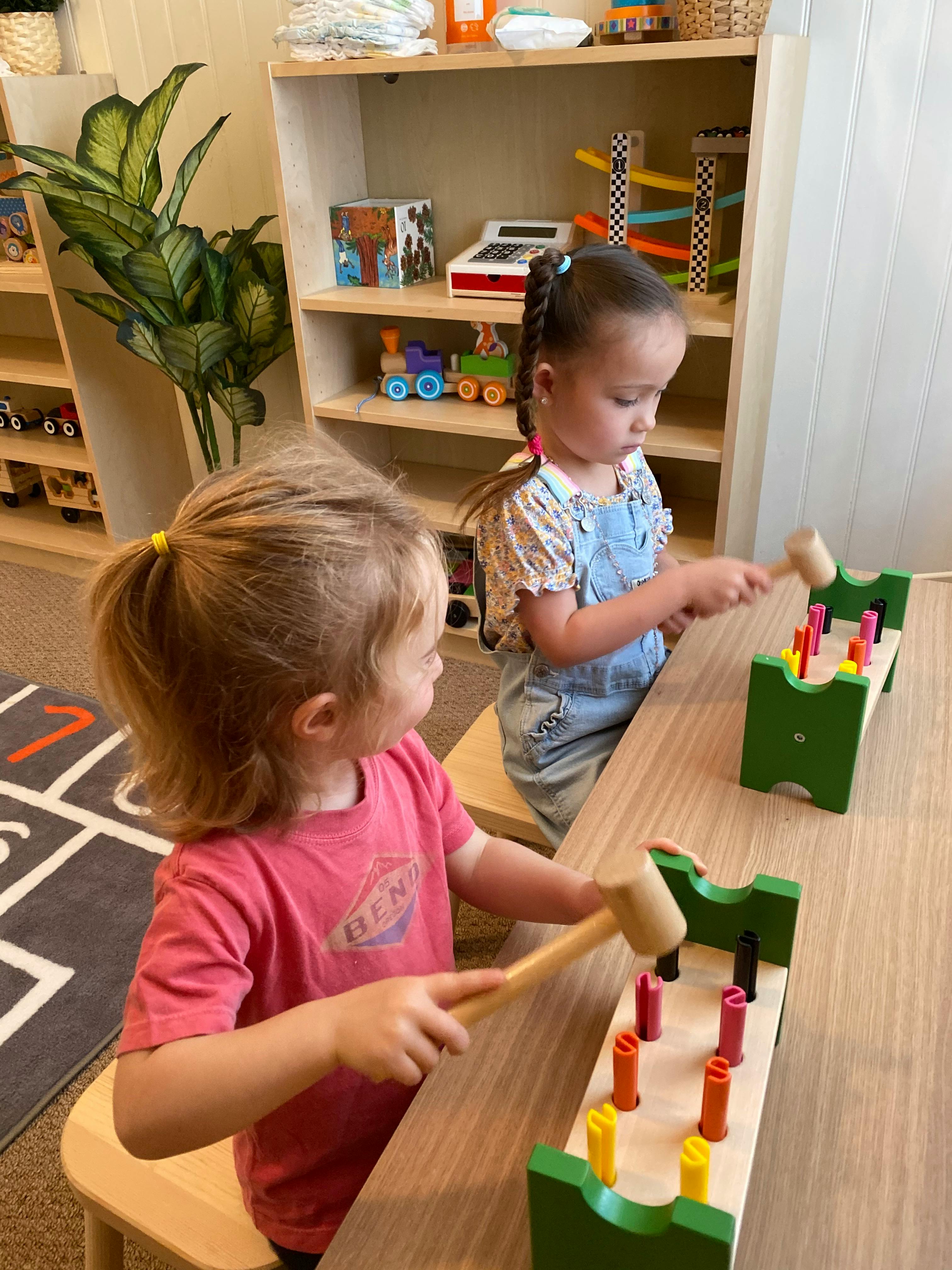 Two children playing with hammer and peg toys at a table